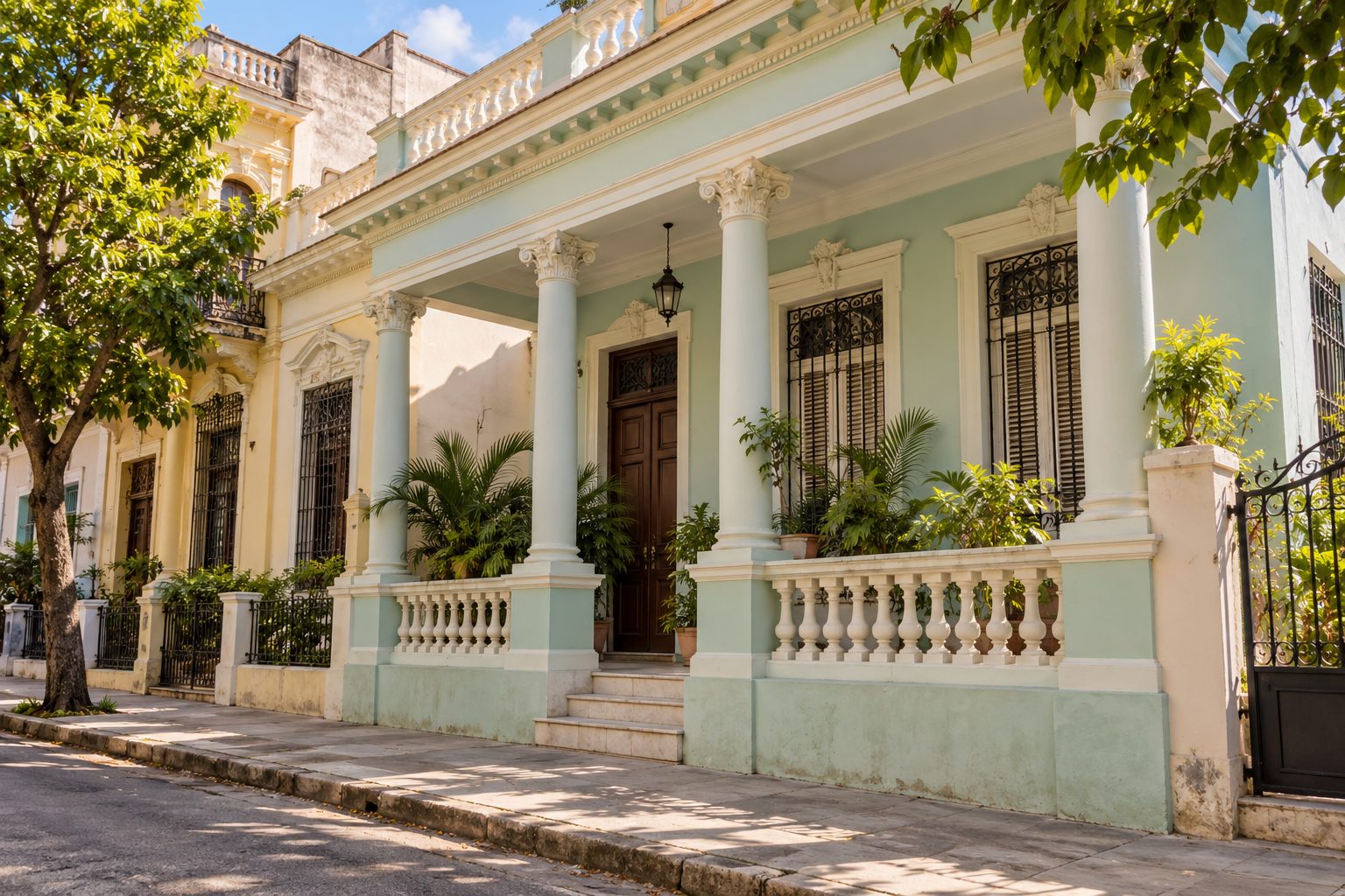 Fachada de una vivienda de estilo cubano con columnas, portal y ventanas altas en una calle tranquila